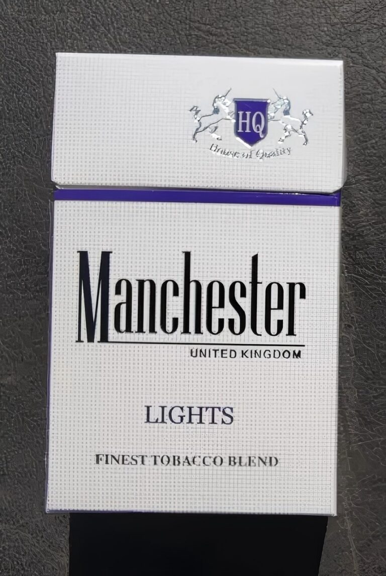 Front of a Manchester Light Blue cigarette pack photographed on a black textured surface